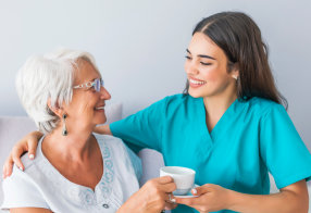 senior woman holding a cup and caregiver holding plate smiling
